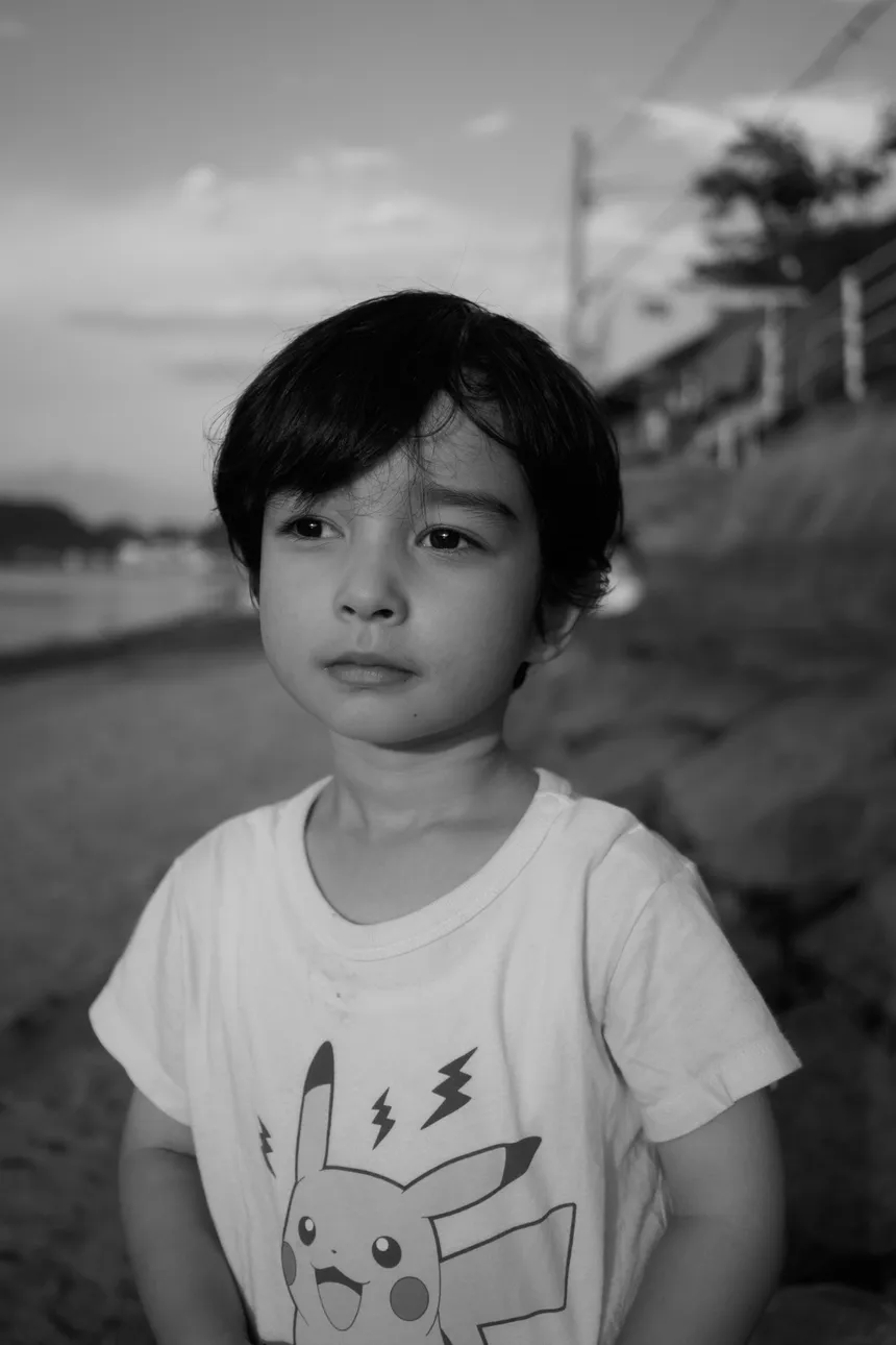 Retrato en blanco y negro de Akito en la playa de Mukaishima, mirando fuera de cámara con una camiseta de Pikachu.