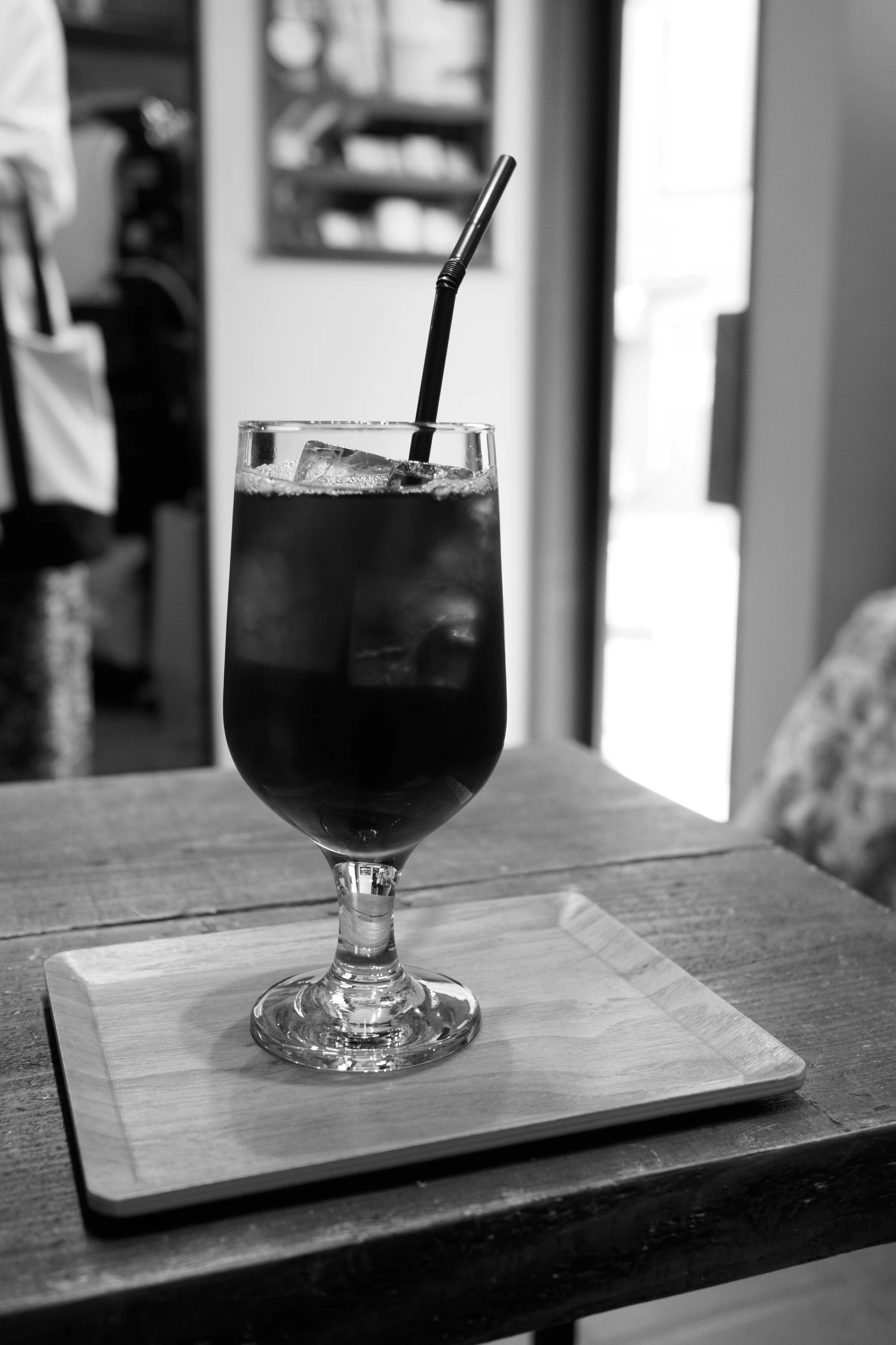 Un vaso con un refresco oscuro, hielo y una pajita metálica sobre una bandeja de madera.