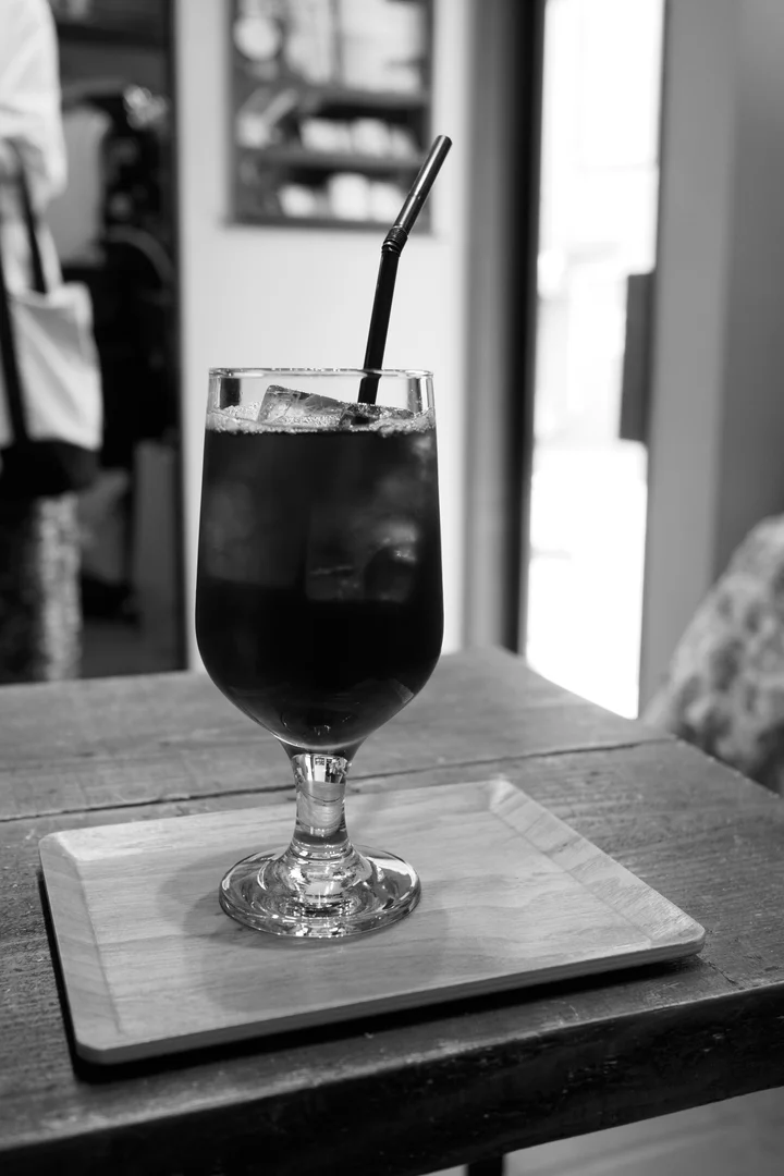 Un vaso con un refresco oscuro, hielo y una pajita metálica sobre una bandeja de madera.