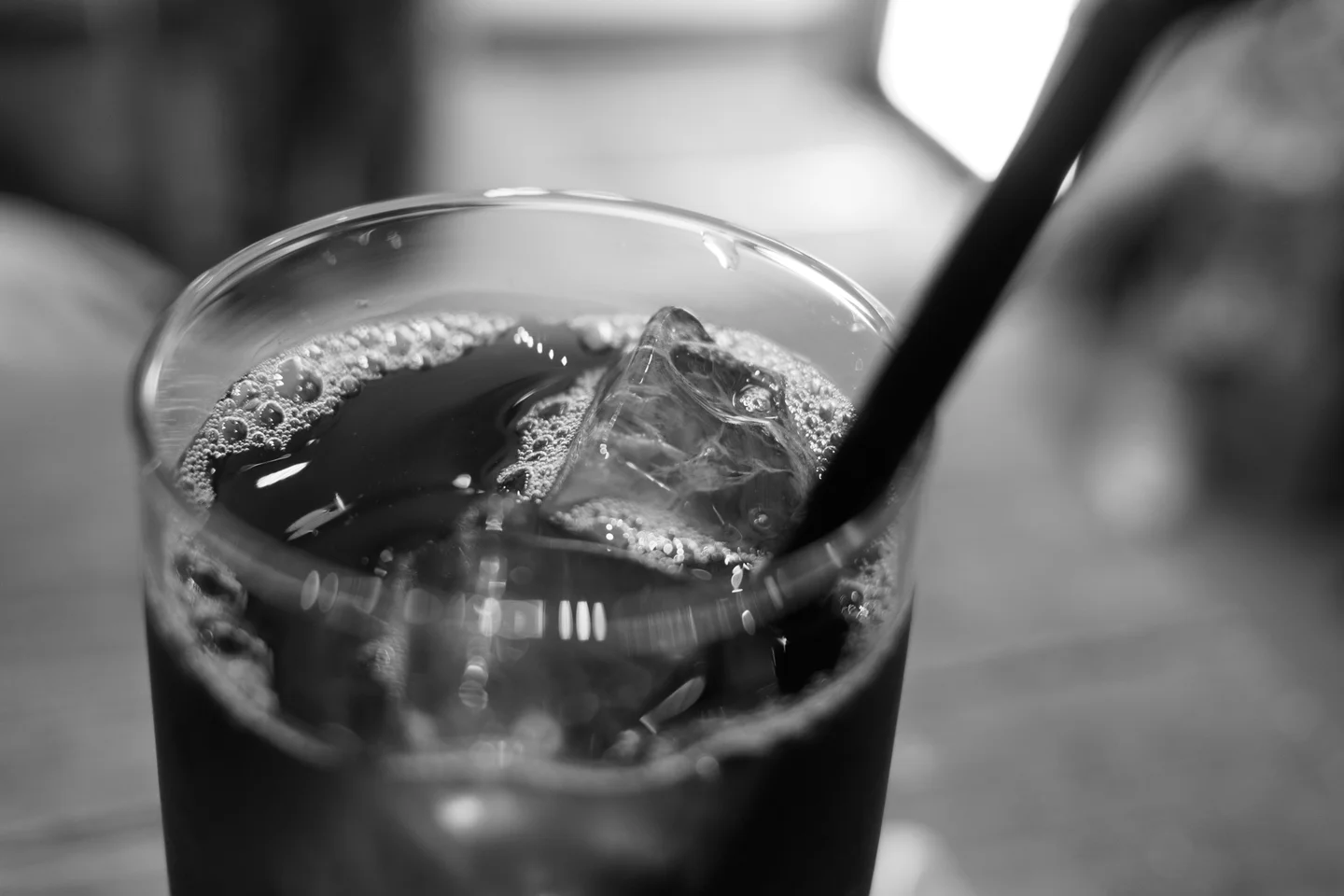 Primer plano de un vaso con refresco de cola, un cubito de hielo y una pajita metálica.